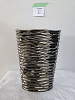 Front view of modern pottery vase with silver painted wavy textured surface on white fabric background