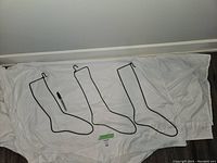 Three black metal wire sock stretchers laid flat on white cloth showing varying sizes.