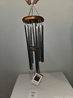 Front view of Woodstock Chimes of Kyoto wind chime showing wooden top, metal tubes, wooden striker, and hanging strings with brand tag attached.