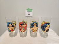 Full front view of all four Wonder Woman collector glasses in different iconic poses with colorful artwork and gold accents.