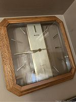Oak framed Bulova quartz wall clock with vertical striped face and silver hands shown on wall.