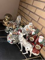 Photo shows an assortment of Christmas-themed décor including several snow globes with holiday scenes and nine figurines featuring Santa Clauses, a white deer, and a chef figure.