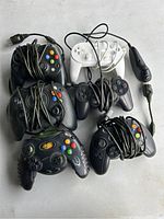 Seven assorted wired video game controllers with visible cables, placed together on a white surface.