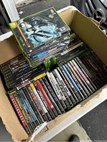 Box containing multiple Xbox and Xbox 360 game cases attracting various genres and titles