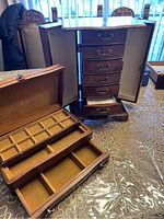 Photo showing two wooden jewelry boxes, one a tall cabinet with drawers and side compartments, the other a smaller box with trays and compartments.