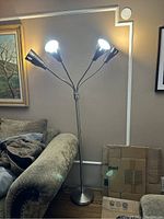 Metal floor lamp with three lit cone-shaped adjustable lamps, silver finish, round base, photo taken from side angle.