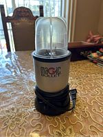 Magic Bullet blender base with power cord, clear blending cup mounted with blade assembly inside, plastic lid on top