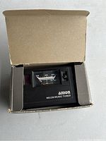 Arion Micon Music Tuner device placed inside the original box, showing the front with analog meter and brand name.