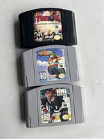 Three Nintendo 64 game cartridges shown stacked on a white background: Turok: Rage Wars (black cartridge), Wave Race 64 (gray cartridge), NHL Breakaway 98 (gray cartridge).