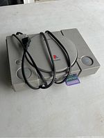 Sony PlayStation 1 console on white surface with power cable wrapped around and memory card inserted