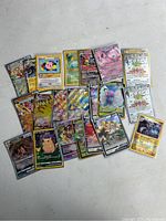 A photo showing 18 rare and holographic Pokemon trading cards laid out on a flat surface including characters such as Mimikyu, Pikachu, Mew EX, Venonat, Umbreon GX, and other shiny cards.