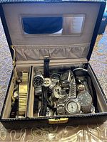 Top view of several assorted wristwatches in a storage box lined with grey velvet and a mirrored lid.