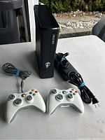 Xbox 360 console with two controllers and the power supply on a white surface.
