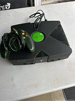 Original Xbox console with two wired translucent green controllers and power cable shown on table.