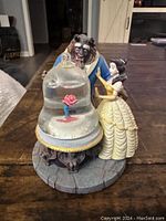 Front view of the Beauty and the Beast snowglobe figurine showing Beast and Belle with the rose encased in a glass dome on a stone-like base.