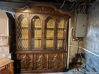 Image of a large wooden china closet cabinet with glass doors and detailed carved wood panels at the bottom.