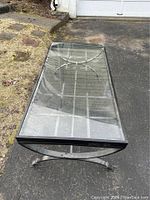 Rectangular coffee table with glass top and metal frame photographed outdoors on asphalt. Shows clear condition and design of the metal base and glass surface.