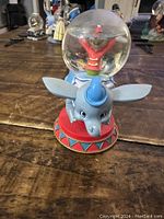 Photo of Dumbo snowglobe showing the blue elephant base with large ears and the glass globe containing a figure in a red outfit.