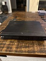 Black LG DVD player on wooden table, showing front and top surfaces with LG branding and logos.