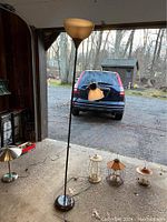 Room scene with five lighting items: one tall floor lamp and four smaller lantern accent lamps placed on the floor in front of a garage opening.