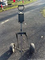 Front view of the black metal golf bag cart showing two solid wheels, adjustable handle, and securing straps.