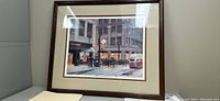 Framed painting showing a vintage city street scene with clock tower, storefront, group of pedestrians, and streetcar.
