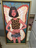 Framed painting showing a woman with butterfly wings, giraffe print top, zebra print shorts, and a blue dotted background.