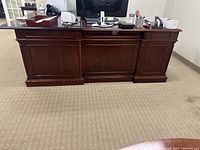 Front view of one reception desk showing dark polished wood, panel details, and occupied with office items (not included).