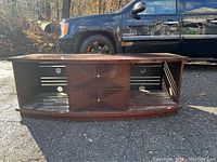 Wooden TV stand outside on pavement with two drawers, two open side shelves with cable holes.