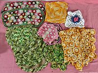 Full view of lot showing assorted crocheted linens in a variety of colors and patterns placed on a pink fabric background.