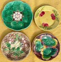 Four antique majolica plates laid out on yellow cloth, showing different floral and leaf designs.