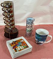 Stacking coffee cups on metal holders, square plates with San Antonio design, and nature-themed Loon mug displayed on a table.