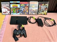 Front view of PS2 slim console, controller, power adapter, AV cable and five front-facing game cases