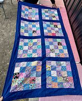 Full view of the handmade vintage cotton patchwork quilt showing eight patchwork blocks with solid blue sashing and border, laid out flat and held by a person.