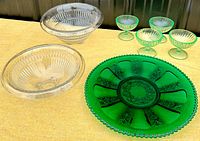 Photo showing all items in the lot including four green uranium glass footed dessert cups, two clear glass mixing bowls, and one emerald green depression glass serving plate.