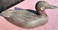 Front and side view of vintage wood duck decoy showing carved feather details, painted eyes, and ribbon tied around the neck. Visible wear on paint.