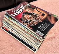 Stack of 20 plus vintage National Lampoon magazines seen from angled side view showing spines and covers in a pile