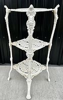 Front view of ornate three tier white cast iron plant stand showing overall structure and detailing.