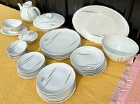 Photo shows entire dish set laid out on yellow cloth with teapot, lidded casserole, gravy boat, various plates and bowls, large oval platter all with modern tree pattern.