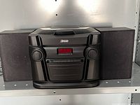 Front and angled views of the 3 CD changer stereo system with speakers on a shelf, showing the digital display, control knobs, and speaker design.