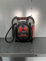 Front view of the Vector 12V battery charger and jump starter showing the control panel with red and black battery clamps attached.