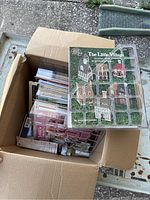 Top view of an open cardboard box filled with various craft magazines and booklets including 'The Little Village' project featuring miniature house patterns.
