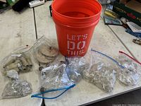 Overall view of orange bucket with multiple bags of crystal chandelier parts and metal fittings laid out around it on a table.