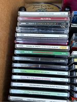 View of the stacked Christmas music CDs inside a bankers box showing the titles and artists of the CDs.