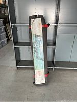 Full view of the Coleman canopy in its gray carrying bag with red straps against metal shelving.