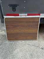 Closed folding card table showing wood-grain laminate top, metal edges, and carry handle.