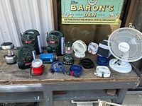 Wide view of lanterns mixed with fans on worn wooden shelf showing overall quantity and type of items.
