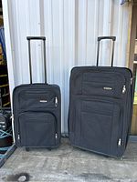 Two black suitcases with telescoping handles standing side by side against a wall, showing their overall appearance.