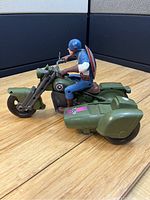 Side view of Captain America figure mounted on olive green motorcycle with sidecar