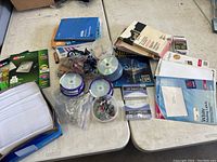 Photo showing the entire lot on a table with various office supplies including paper products, CDs/DVDs, clips, envelopes, and other materials.